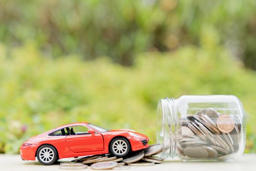 Red car on jar of coin on blurred green natural background. Saving money and investment concept.