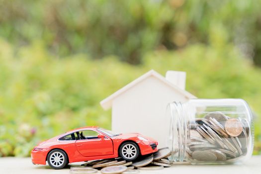 Jar of coins and red car on pile of coin on blurred green natural background. Saving money and investment concept.