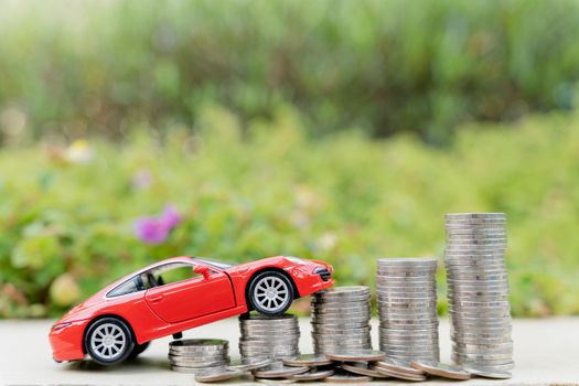 Red car on stack of coin on blurred green natural background. Saving money and investment concept.