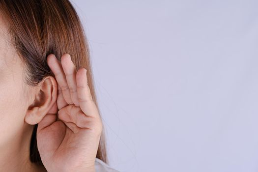woman hearing loss or hard of hearing and cupping her hand behind her ear isolate grey background, Deaf concept.