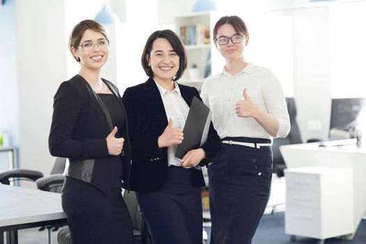 Three young successful business women in the office smiling happily. 