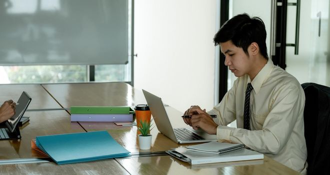 Male office worker browsing in laptop for necessary information, Young asian businessman working at office.