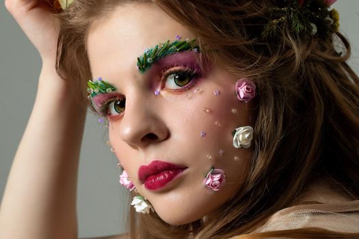 Portrait of a beautiful girl with fantastic summer makeup. Spring girl in flowers. The face of a luxurious model with extended eyebrows and eyelashes. Beauty Salon Concept.