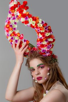 Beautiful girl with flower horns. Spring model. Beautiful girl with an unusual make-up. Hairstyle with flowers. Fantastic portrait of a beautiful woman. Summer fairytale woman. Malificent style.