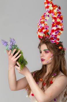 Beautiful girl with flower horns with a bunch of flowers. Malificent. Spring beauty. Woman with summer make-up.