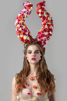 Beautiful girl with flower horns. Spring model. Beautiful girl with an unusual make-up. Hairstyle with flowers. Fantastic portrait of a beautiful woman. Summer fairytale woman. Malificent style.