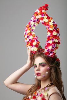 Beautiful girl with flower horns. Spring model. Beautiful girl with an unusual make-up. Hairstyle with flowers. Fantastic portrait of a beautiful woman. Summer fairytale woman. Malificent style.