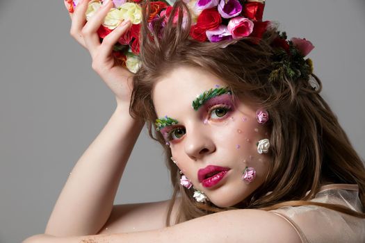 Portrait of a beautiful girl with bright spring make-up. Summer girl in flowers. The face of a gorgeous beauty with extended eyebrows and eyelashes. Natural cosmetics concept.
