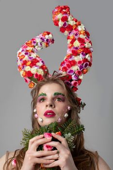 Portrait of a beautiful girl with flower horns. Goddess Flora. Beautiful woman with fantastic makeup and a forest bouquet. Spring girl model.