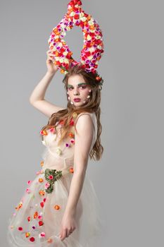 Fairytale girl model with floral horns on a gray background. Maleficent. Spring girl. Woman flower. Floral makeup. Summer woman.