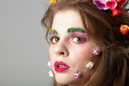 Portrait of a beautiful girl with creative make-up. Summer girl. The face of a luxurious model in flowers. Natural cosmetics concept.