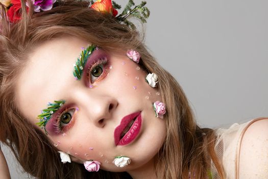 Portrait of a beautiful girl with unusual makeup. Spring girl. The face of a luxurious model in flowers. Eyebrow and eyelash extensions.