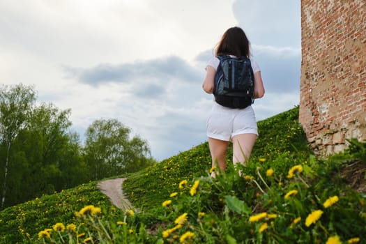 Woman walking along brick wall of a castle on a summer day.