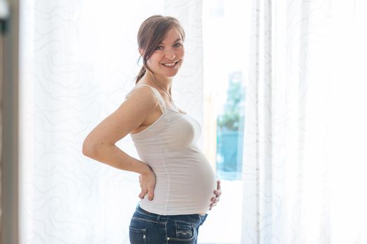 Happy Caucasian pregnant mother touching her tummy, blue jeans, close up