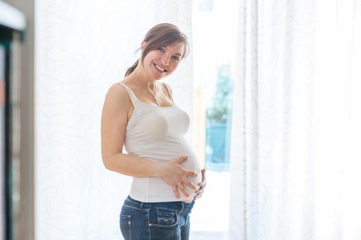 Happy Caucasian pregnant mother touching her tummy, blue jeans, close up