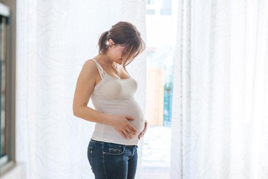 Happy Caucasian pregnant mother touching her tummy, blue jeans, close up