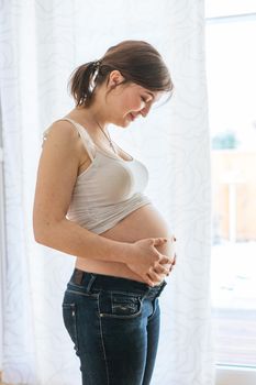 Happy Caucasian pregnant mother touching her naked tummy, blue jeans, close up