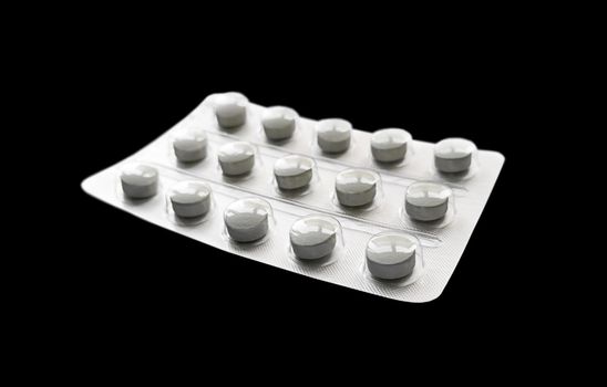 Grey pills in blister isolated on a black background.