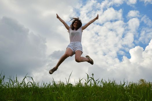 Happy girl jumping against the background of blue sky and clouds.