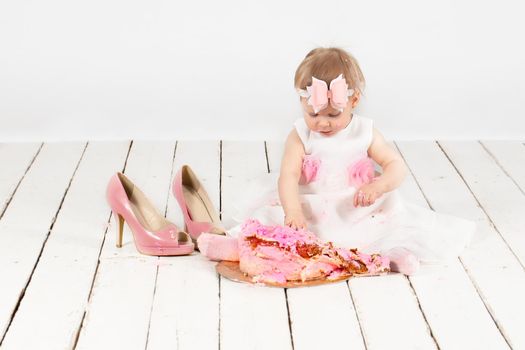 Little funny year-old girl with a festive cake, smeared with cream, is sitting on the floor.