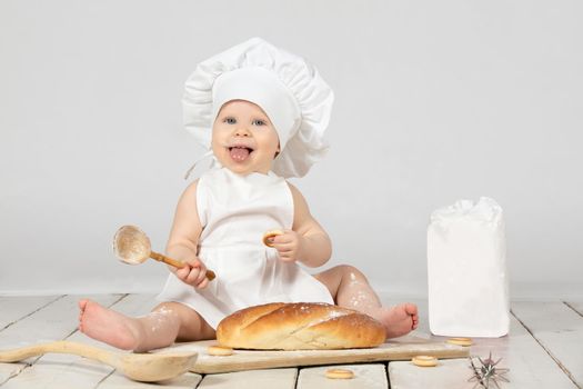 Child cook. Beautiful little girl in cook clothes with long loaf and flour. The child is one year old. Funny baby is laughing. Little chef. The concept of baking bakery products.