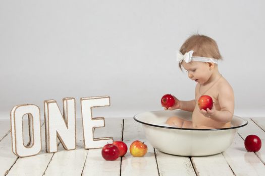 Beautiful one-year-old girl bathes in a basin. Photoshoot on your first birthday.