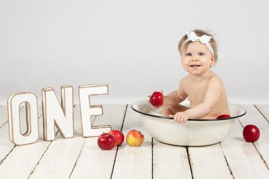 A happy child bathes in a basin. Beautiful little girl in one year. Little one with letters.