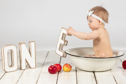 Beautiful one-year-old girl bathes in a basin. Photoshoot on your first birthday.