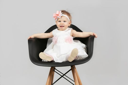 The child is one year old. Beautiful little girl is sitting on a chair. Funny child with a bow. Charging baby.