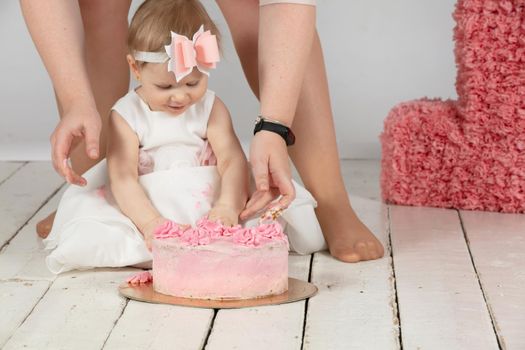 The child’s birthday is one year. Mom’s hands and a beautiful baby. Little girl with a birthday cake.