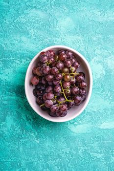 Fresh ripe grape berries in bowl on turquoise textured background, top view