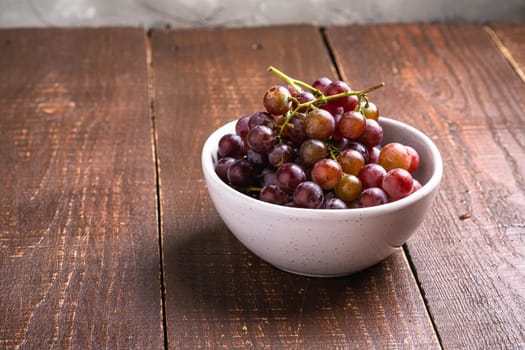 Fresh ripe grape berries in bowl on brown wooden table, angle view