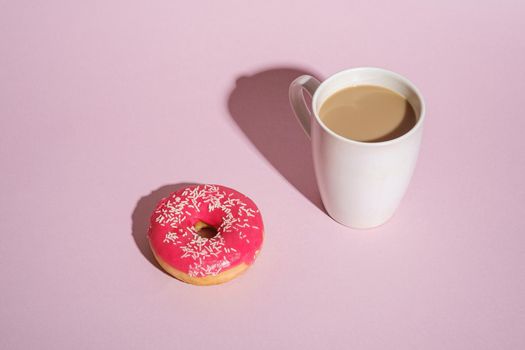 Pink donut with sprinkles near to cup of coffee, sweet glazed dessert food and hot drink on pink minimal background, angle view copy space