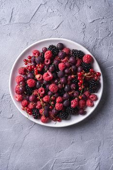 Tasty fresh ripe raspberry, blackberry, gooseberry and red currant berries in plate, healthy food fruit on stone concrete background, top view