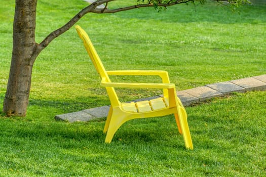 Yellow chair on green lawn in a tree shadow.