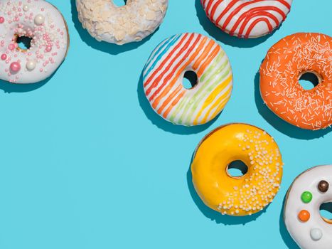 Delicious glazed donuts on blue background. Flat lay - set of different colorful donuts or doughnuts on blue with copy space edge. Bright sun light with hard shadows