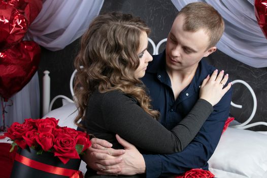 Loving couple from top to bottom. Man and woman with red roses in the bedroom. Beautiful young husband and wife.Close-up man and woman hugging.Valentine's day.