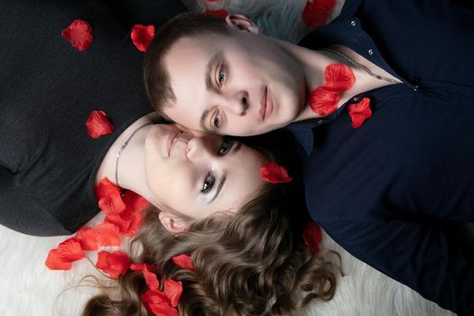 Loving couple. Man and woman lie in rose petals. Beautiful young husband and wife.