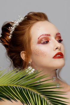 Portrait of a beautiful girl with bright makeup and a tropical leaf. Summer girl. Gorgeous beauty with extended eyebrows and eyelashes. Beauty concept.