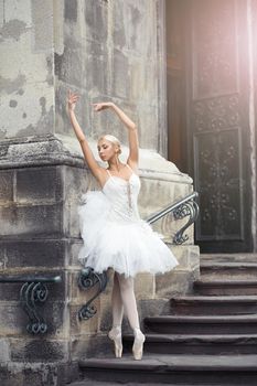 Attractive young female ballet dancer performing outdoors dancing on the stairway of an old fashioned building.