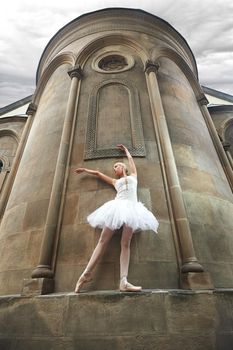 Young female ballet dancer in white outfit performing near epic old castle outdoors.