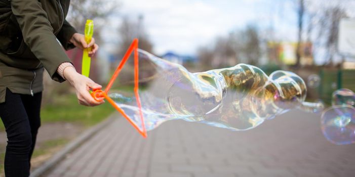 A girl blows soap bubbles in the park for the entertainment of children. Large, colorful soap bubbles in the open air in a public park.