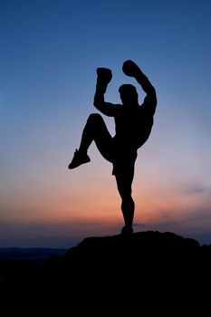 Silhouette of a male boxer practicing Muay Thai outdoors epic sunset scenery on the background copyspace kicking kickboxing boxing fighting training sports motivation nature balance preparing combat.