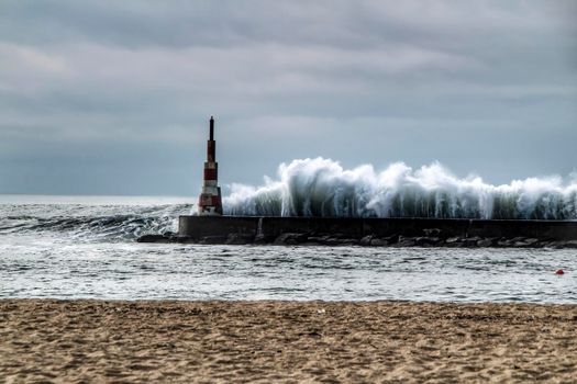 Giant waves breaking on the breakwater and the lighthouse on Aguda Beach, Miramar, Arcozelos town