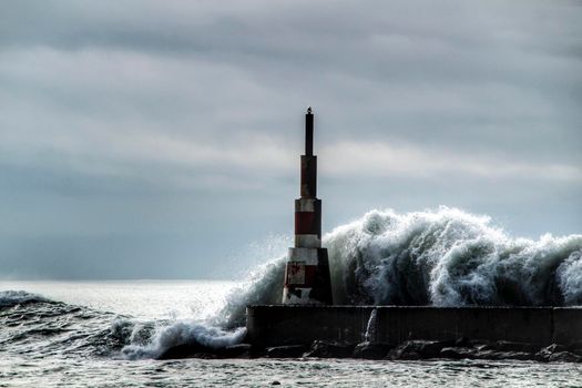 Giant waves breaking on the breakwater and the lighthouse on Aguda Beach, Miramar, Arcozelos town