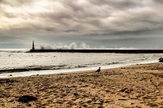 Giant waves breaking on the breakwater and the lighthouse on Aguda Beach, Miramar, Arcozelos town