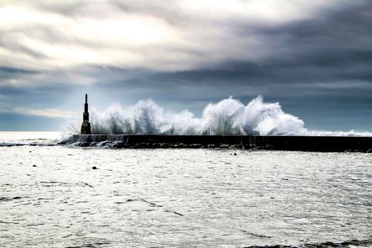 Giant waves breaking on the breakwater and the lighthouse on Aguda Beach, Miramar, Arcozelos town