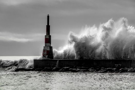 Giant waves breaking on the breakwater and the lighthouse on Aguda Beach, Miramar, Arcozelos town