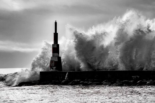 Giant waves breaking on the breakwater and the lighthouse on Aguda Beach, Miramar, Arcozelos town