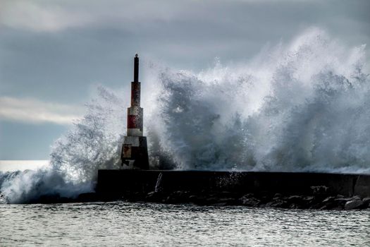 Giant waves breaking on the breakwater and the lighthouse on Aguda Beach, Miramar, Arcozelos town